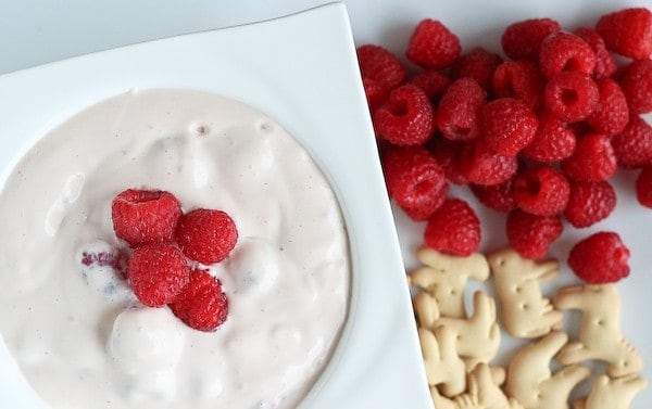 Partial image of dip in square white bowl with raspberries and animal crackers alongside.