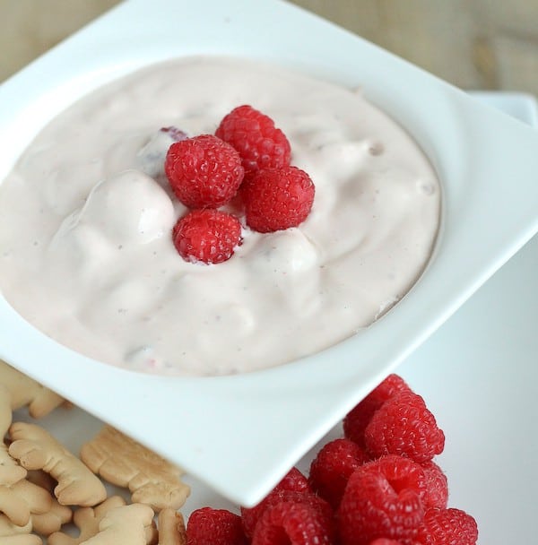 Dip in white bowl garnished with four raspberries.