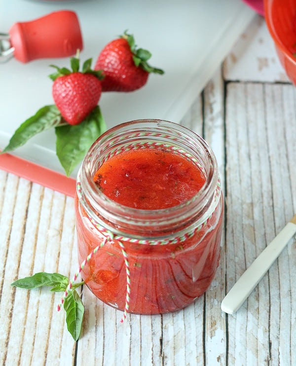 Strawberry basil jam in jar, fresh strawberries and basil in background.