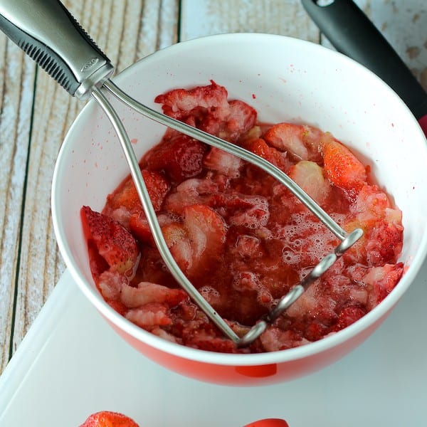 mashed strawberries in bowl, with potato masher