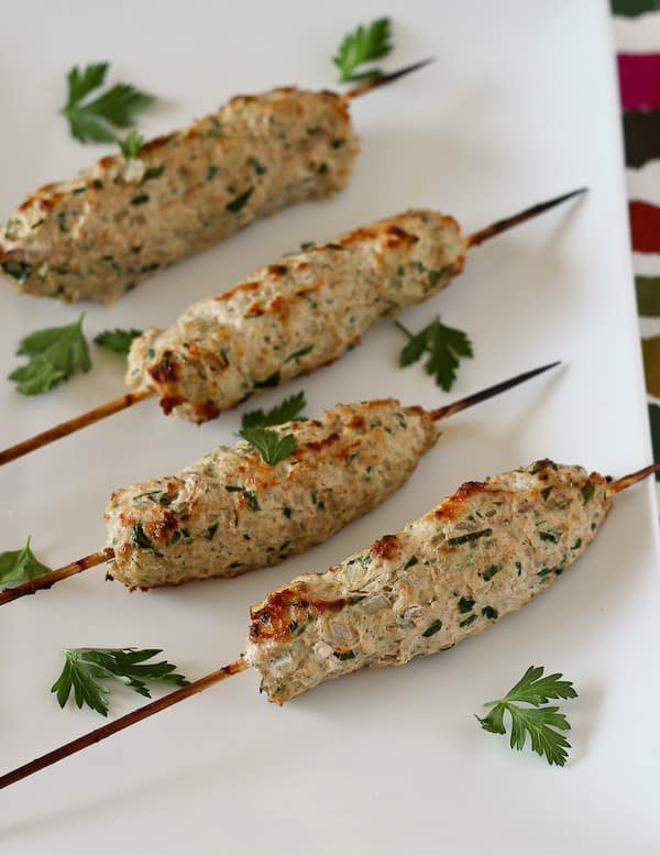 Older photos of four prepared chicken kofta on white plate with garnished with parsley leaves 