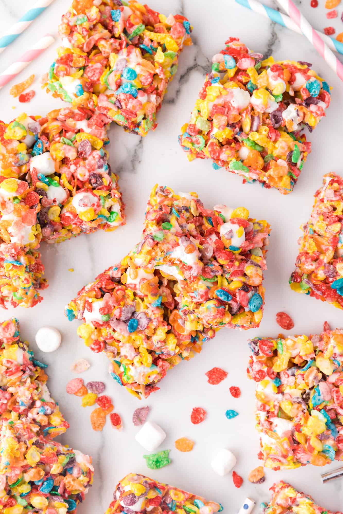 Overhead view of assorted Fruity Pebbles treats scattered on a white surface.