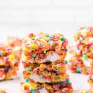 A stack of three Fruity Pebbles treats on a countertop with more treats in the background.