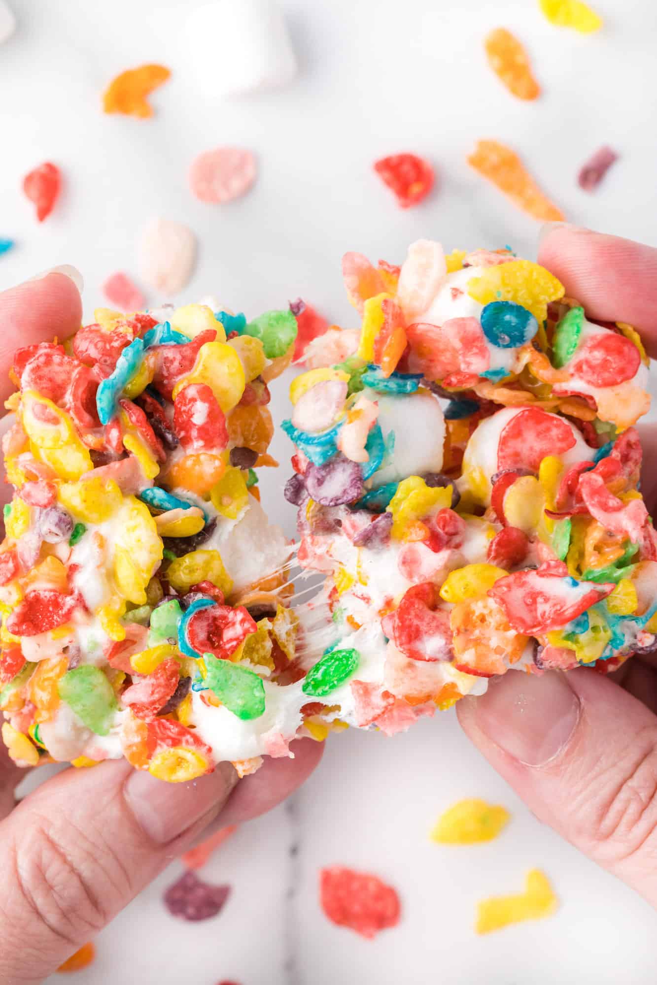 Two hands pulling apart a gooey Fruity Pebbles treat.