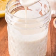 A spoon drizzling tahini sauce into a mason jar.