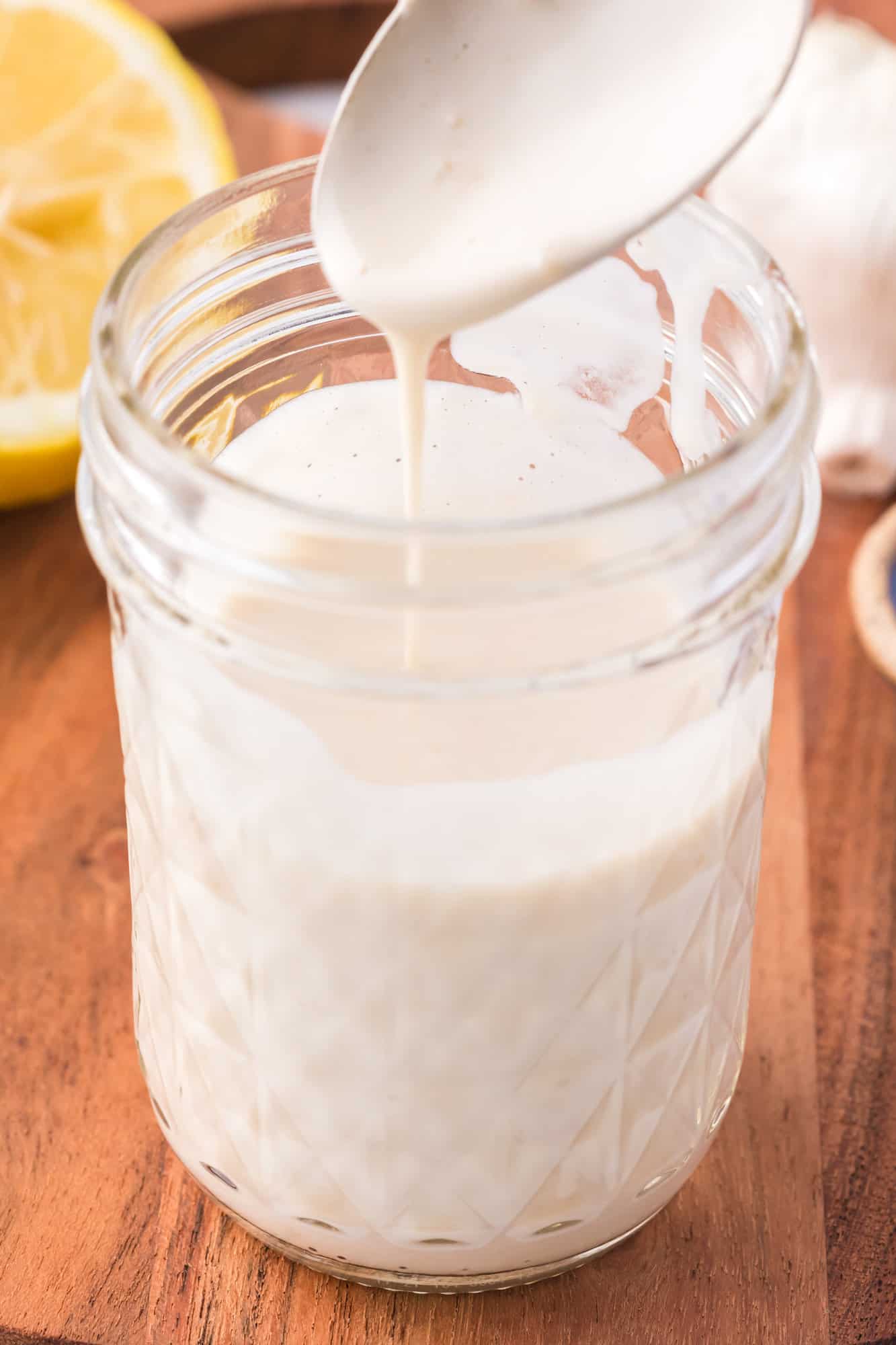 A spoon drizzling tahini sauce into a mason jar.