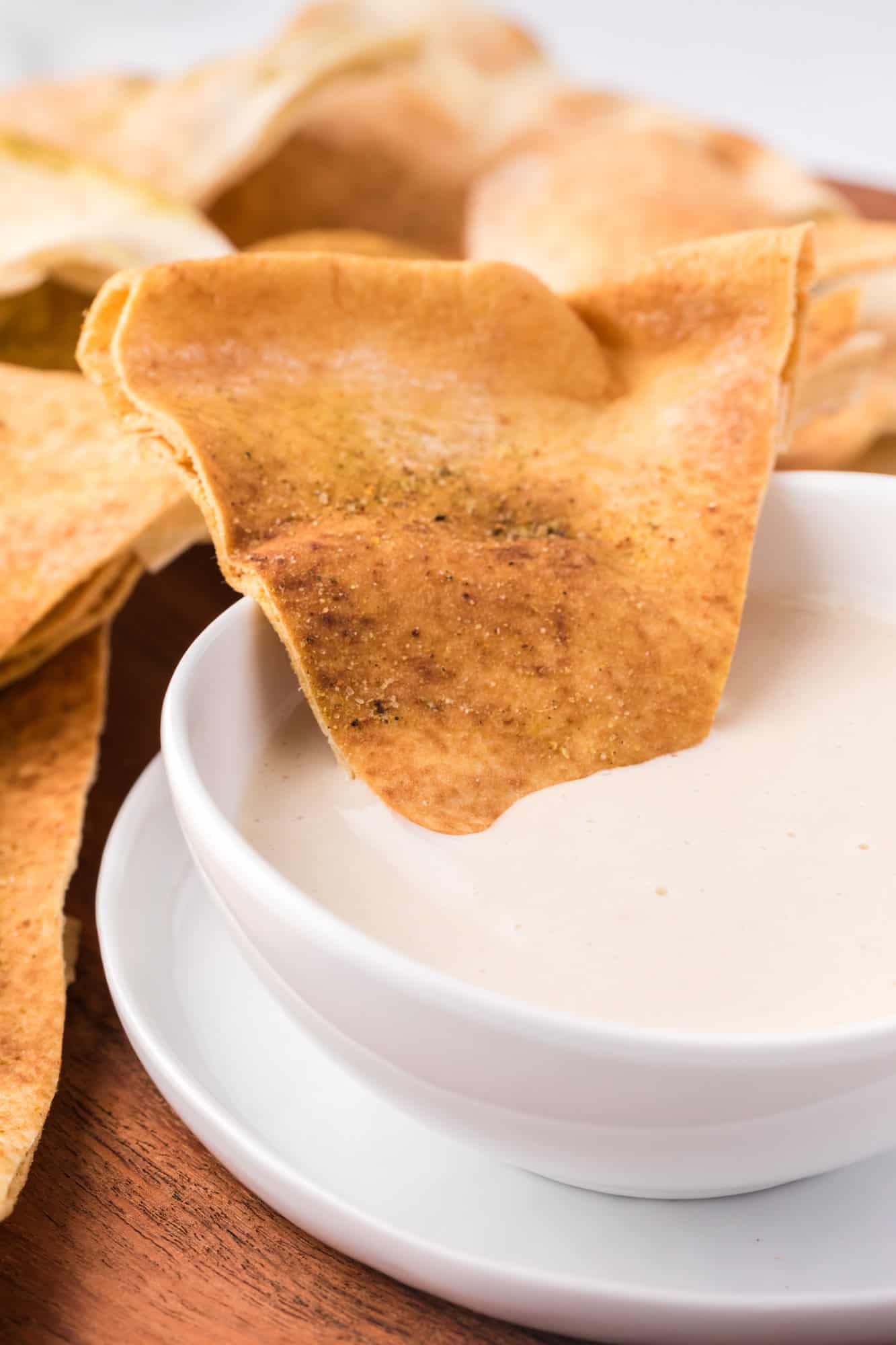 A pita chip resting in a bowl of tahini sauce.