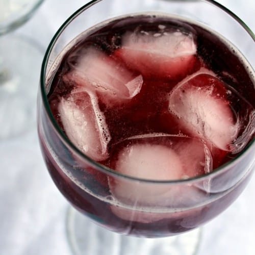 Close up overhead view of red wine spritzer in clear wine glass with 5 ice cubes.