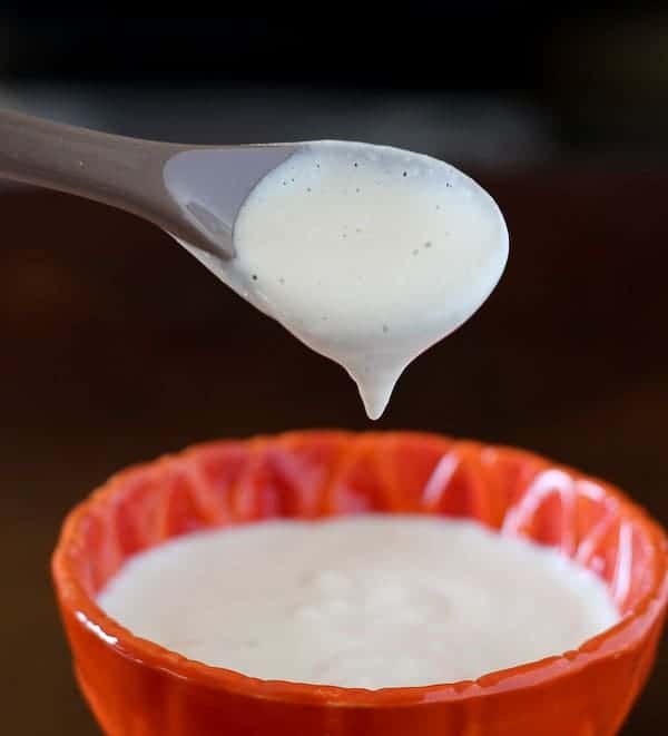 Closeup of sauce dripping from spoon into bowl.