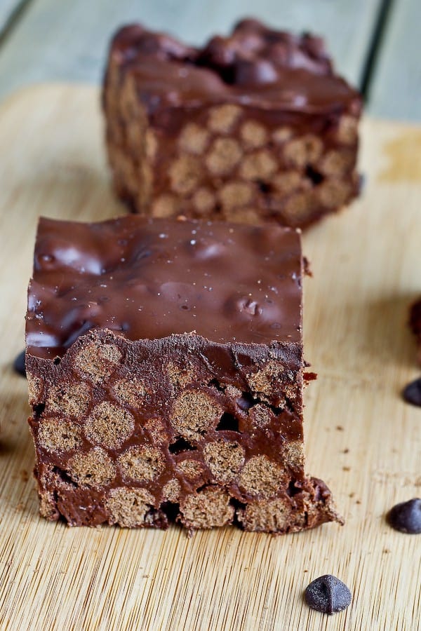 Closeup of two pieces of Cocoa Puff treats on a bamboo cutting board with chocolate chips sprinkled around. 