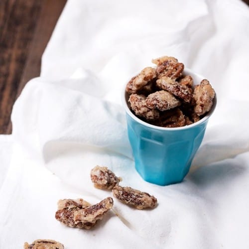 Candied pecans in small blue container on white cloth.