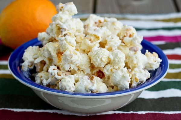 Front view of popcorn piled in shallow blue bowl, orange in background, on striped cloth.