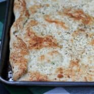 Partial image of cheesy flatbread in baking pan.