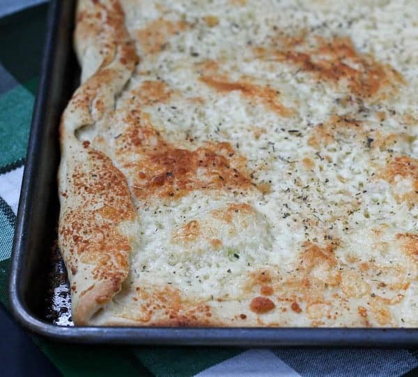 Partial image of cheesy flatbread in baking pan.