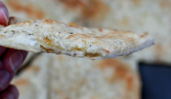 Closeup of slice of cheesy bread, held in fingers.