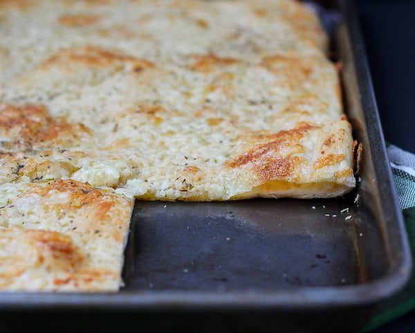 Cheesy flatbread in baking pan with corner piece cut out.