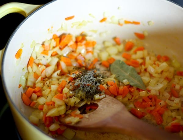 Close up of sauteed carrots and onions in Dutch oven, with dried herbs.
