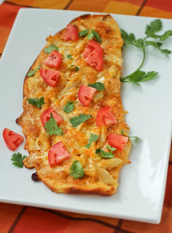 Chicken enchilada flatbread on a white rectangular plate, garnished with fresh cilantro.