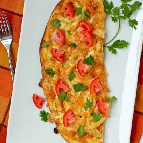 Top view of chicken enchilada flatbread on rectangular white plate, garnished with fresh cilantro.