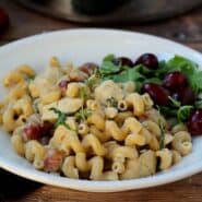 Pasta with grapes and chicken in a white bowl.