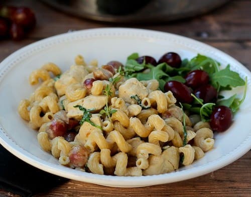 Pasta in shallow white bowl, garnished with fresh arugula and grapes.