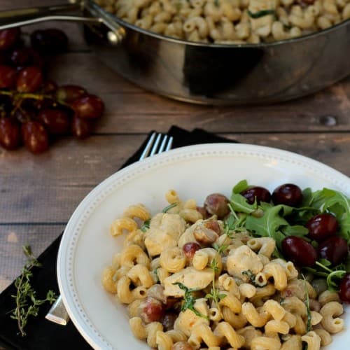 Pasta with grapes and chicken in a white bowl.