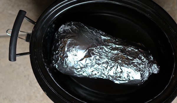 Overhead shot of foil wrapped squash inside crockpot.