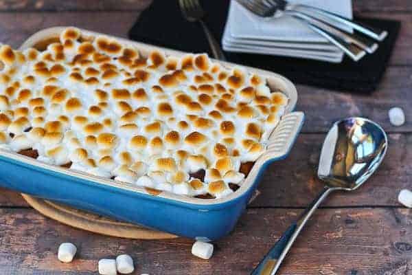 Blue rectangular baking dish containing Sweet Potato Bread Pudding with Marshmallow Topping with serving spoon and mini marshmallows scattered around it.
