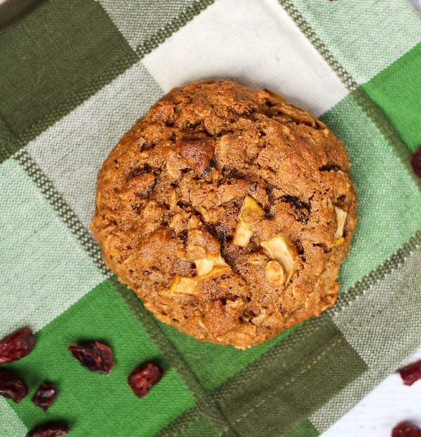 Overhead of gingerbread breakfast cookie on green checked cloth with dried cranberries scattered.