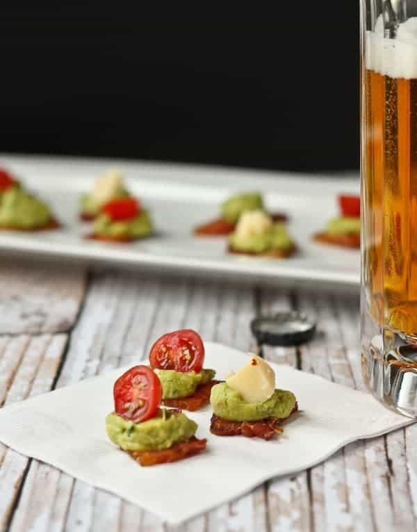 Trio of bacon appetizers on white paper napkin with full beer stein alongside.