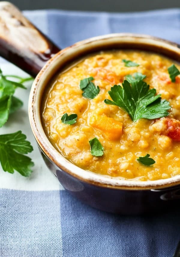 Image of Red Lentil Soup in earthenware bowl with parsley leaves scattered.