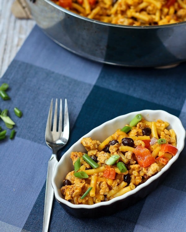 A serving of southwestern mac and cheese in small black stoneware dish with fork along side.