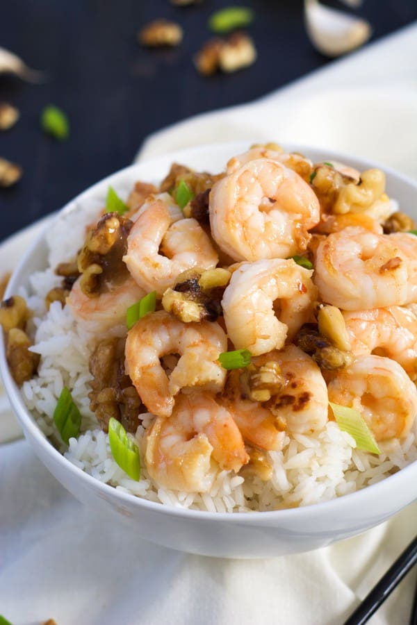 Overhead of shrimp in bowl on white rice, garnished with sliced green onions.