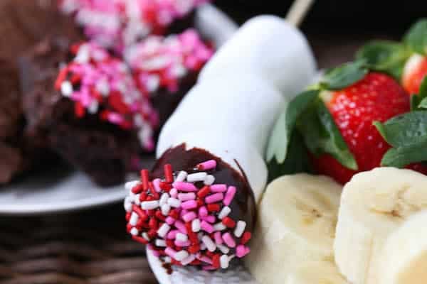 Closeup of large marshmallow dipped in chocolate fondue, and covered with pink and red sprinkles.