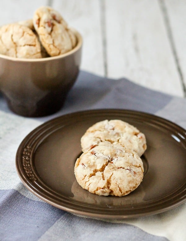 Two cinnamon crinkle cookies on brown plate, a bowl of cookies in background.