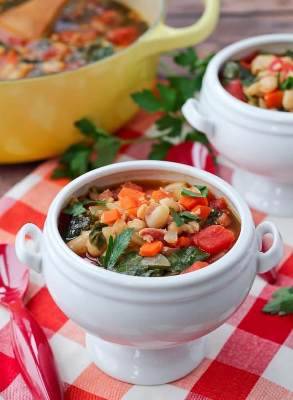 Image of Pancetta and White Bean Soup with Kale in white bowls on red checked fabric.