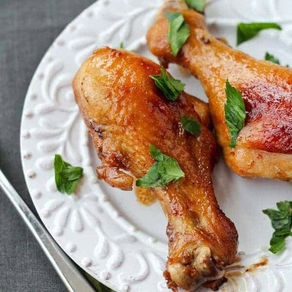 Two drumsticks on white plate garnished with fresh chopped parsley leaves.