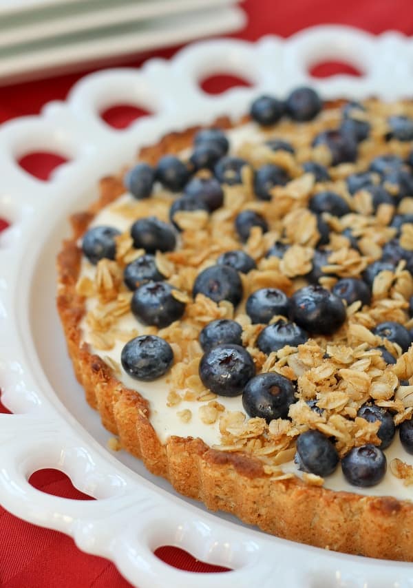 Partial image of tart topped with fresh blueberries and crunchy oat topping on a white decorative plat.