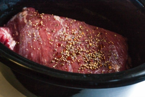 A close up view of uncooked corned beef in slow cooker with spices sprinkled on top.