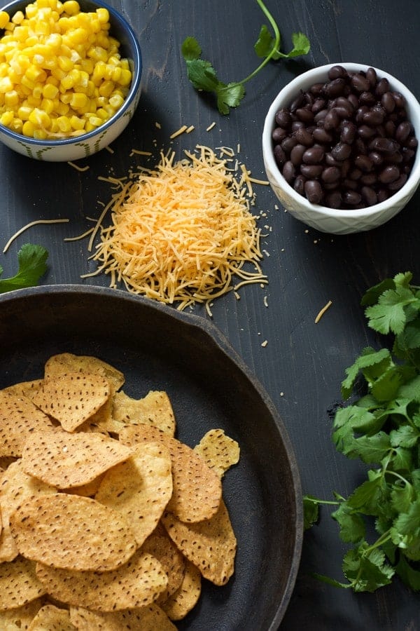 Overhead of nacho ingredients, including chips, cheese, black beans, corn, and cilantro.