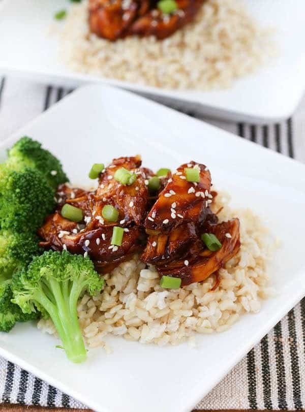 Serving of crock pot teriyaki chicken with broccoli and rice on square white plate.