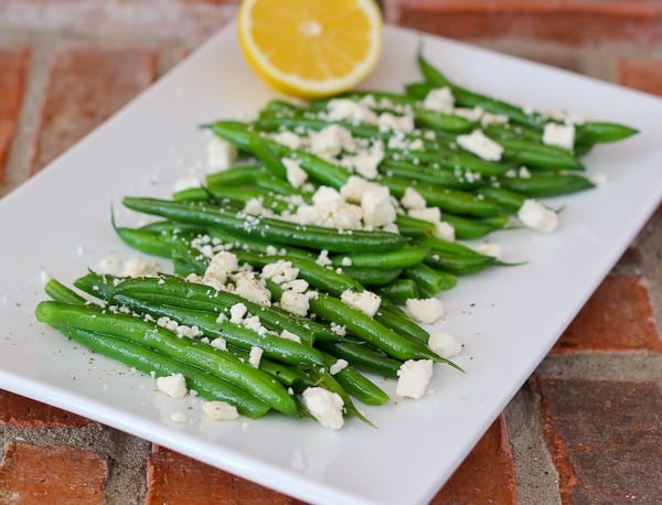 Front view of green beans on platter, placed on red brick background.