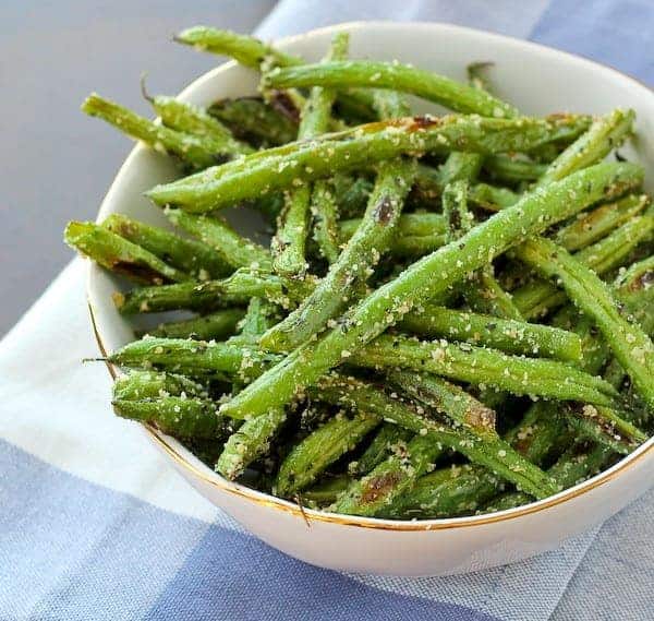 Roasted green beans in decorative white bowl on blue plaid cloth.