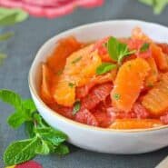 Shallow round white bowl containing citrus salad, garnished with mint.