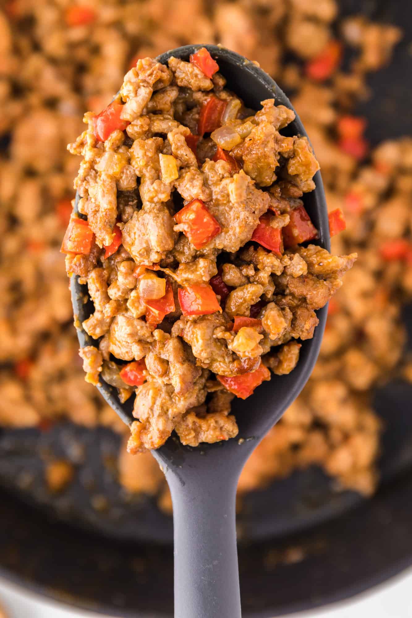 Close up of a spoonful of ground turkey taco meat held over more taco meat in a cast iron skillet.