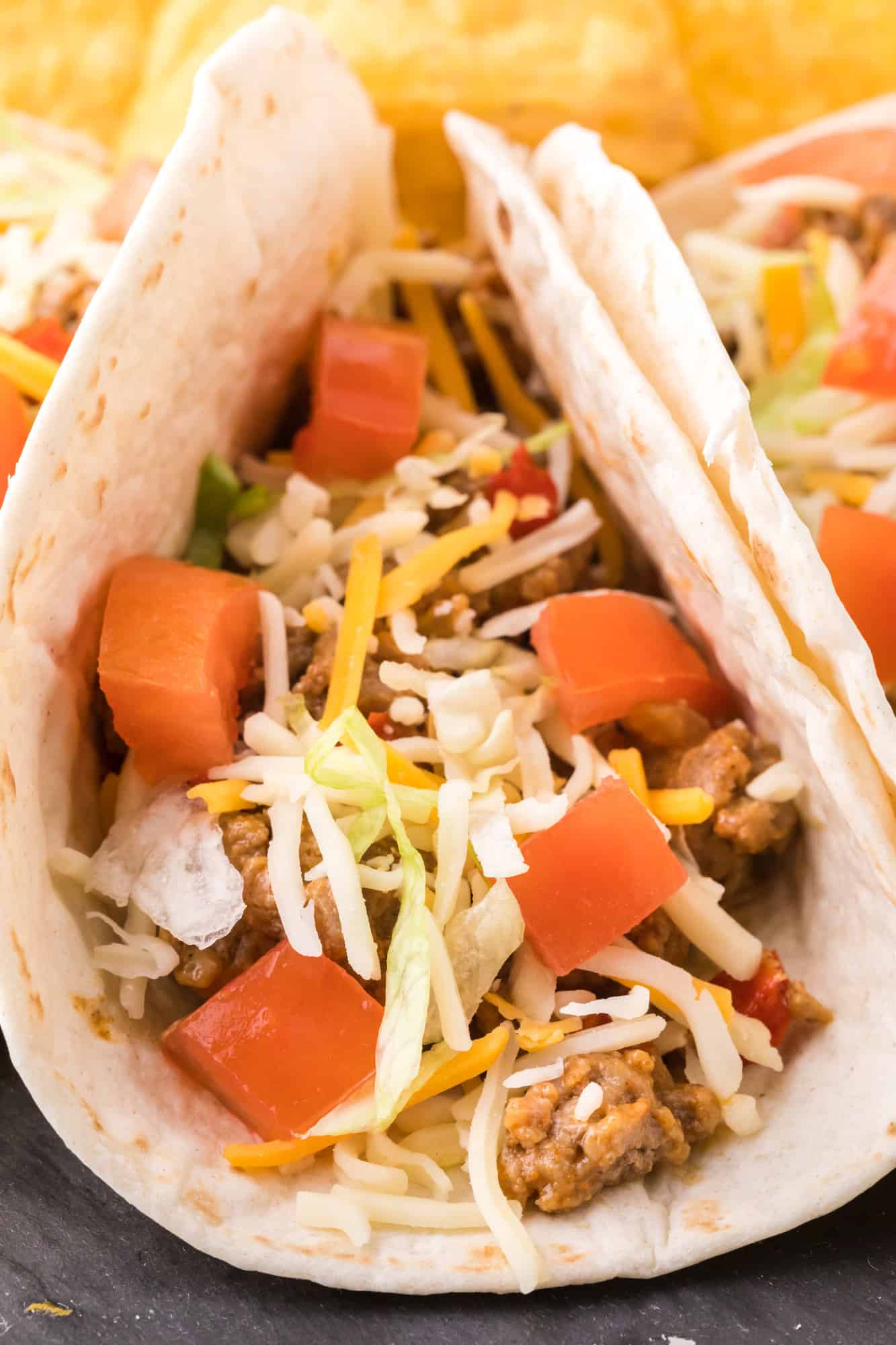 Make the best turkey taco meat packed with zesty Southwestern flavor! Healthy ground turkey tacos are the ultimate easy weeknight recipe. Close up of a soft turkey taco topped with shredded cheese and diced tomatoes.