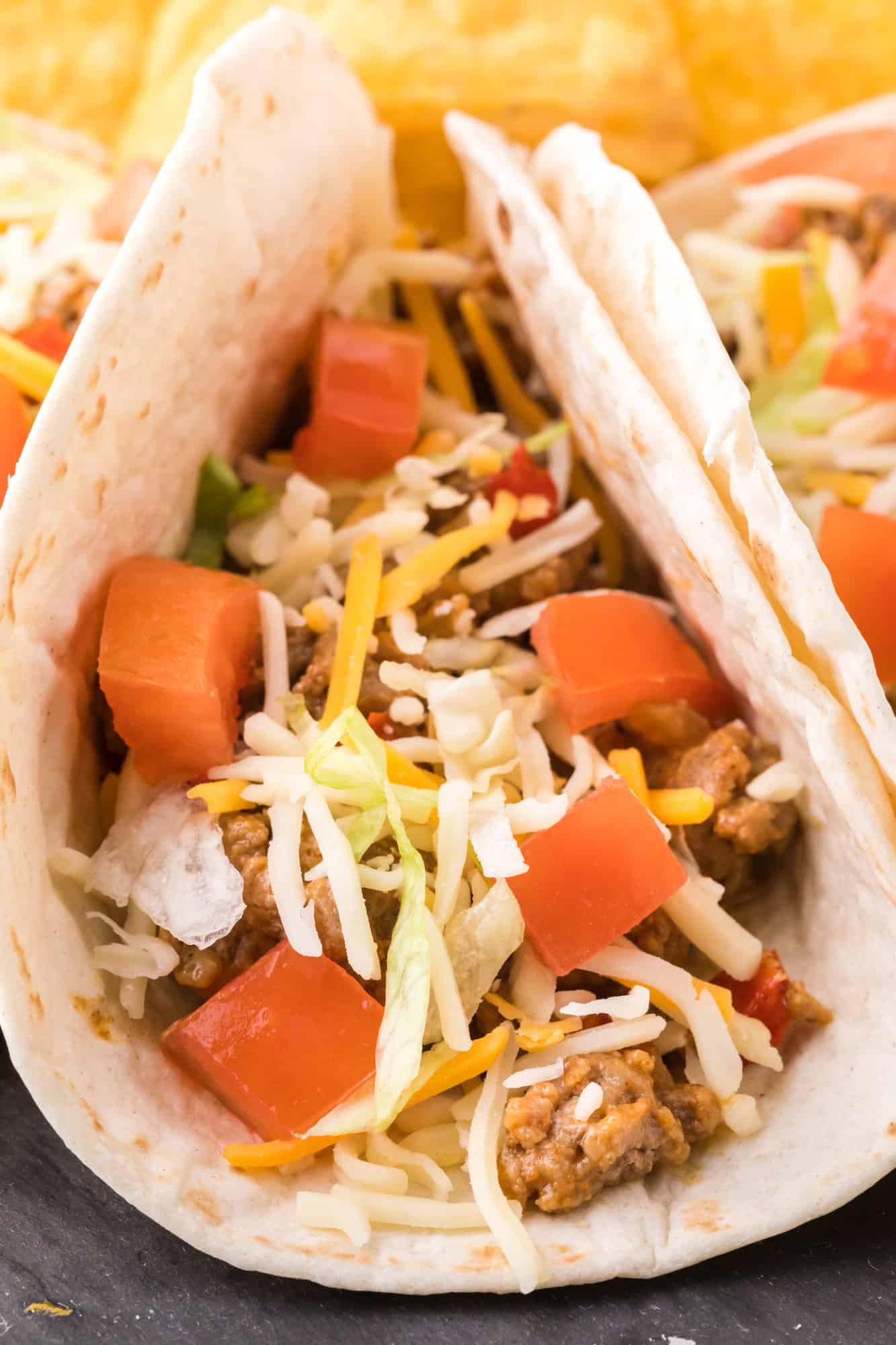 Close up of a soft turkey taco topped with shredded cheese and diced tomatoes.