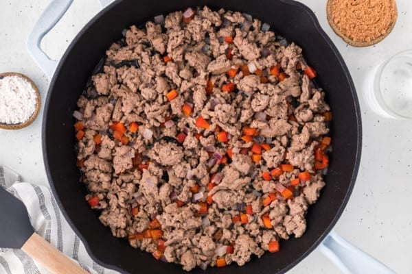 Ground turkey sauteing in a cast iron skillet with diced vegetables.