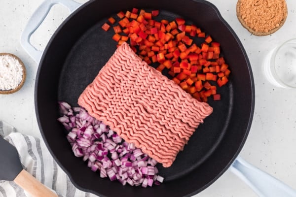 Uncooked ground turkey, diced peppers, and diced onions added to a cast iron skillet.