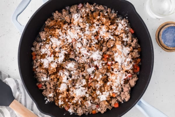 Flour sprinkled over sauteed ground turkey taco meat in a cast iron skillet.